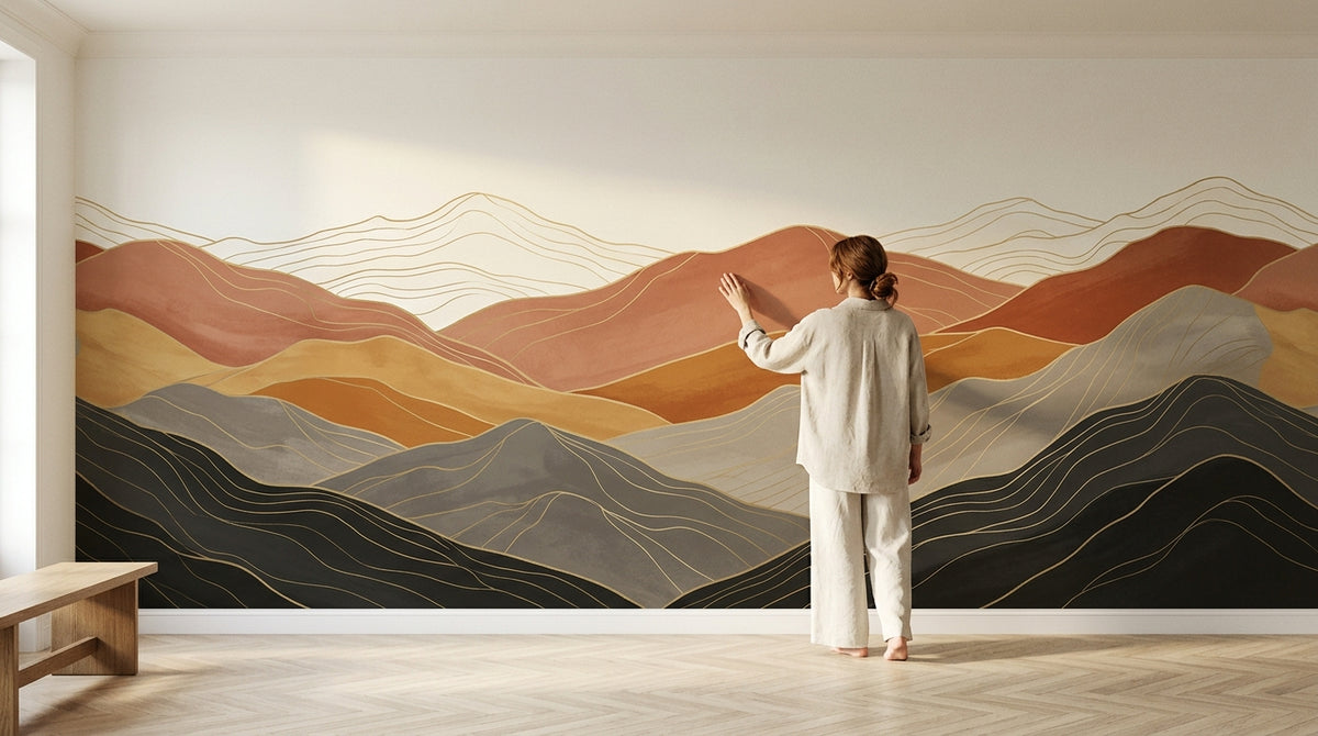 Une femme pose la main sur un papier peint panoramique de montagnes terracotta, ocre et anthracite qui couvre tout un mur